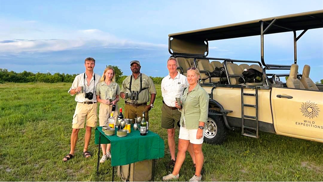 Ingwe Collective guides and guests beside a safari vehicle at sunset